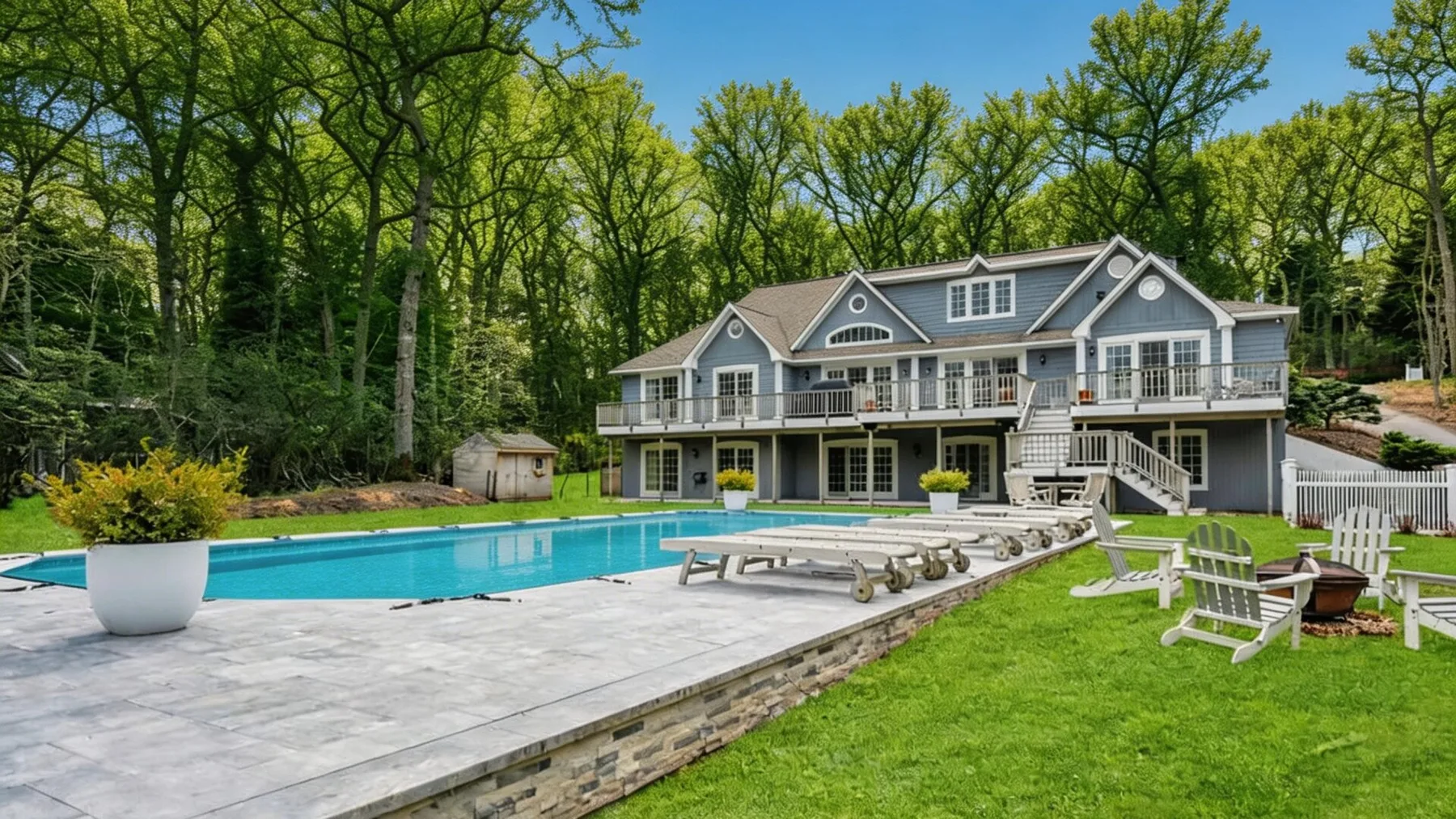 A large house overlooks a swimming pool, with outdoor seating on the lawn.