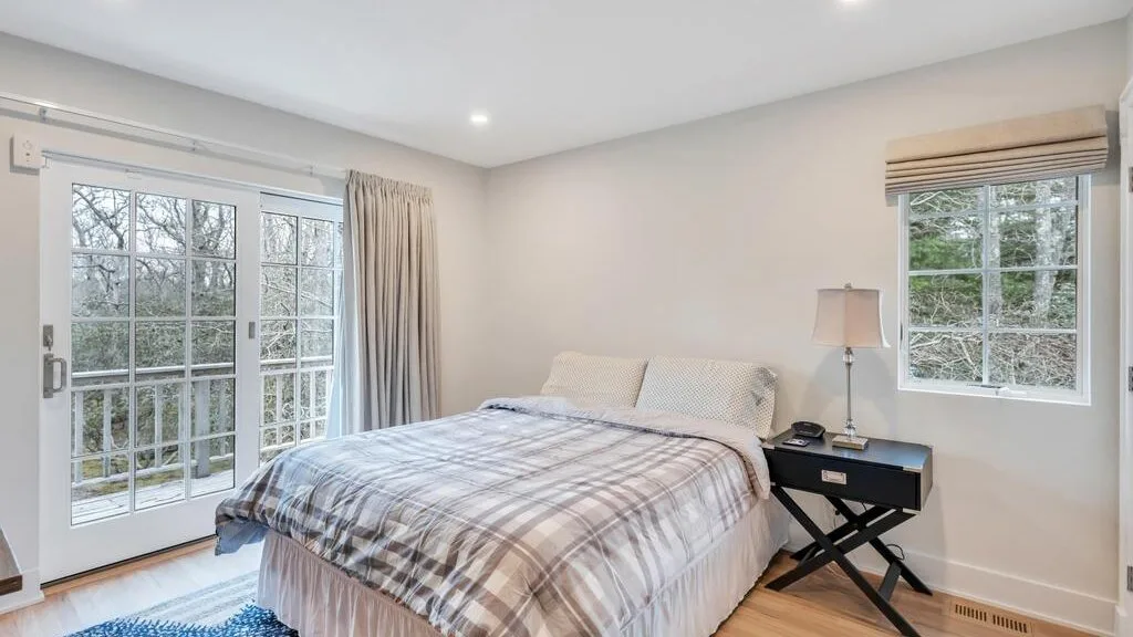 Un dormitorio luminoso con una cama junto a grandes ventanas y una puerta de vidrio.