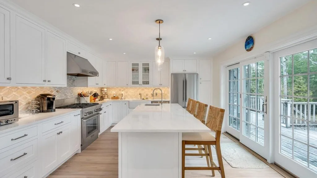 Una cocina luminosa con gabinetes blancos, una isla central y ventanales.