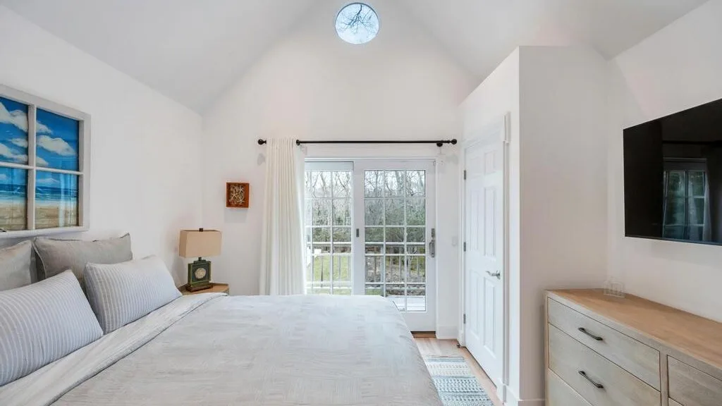 Un dormitorio luminoso con una cama, una ventana y un televisor en la pared.