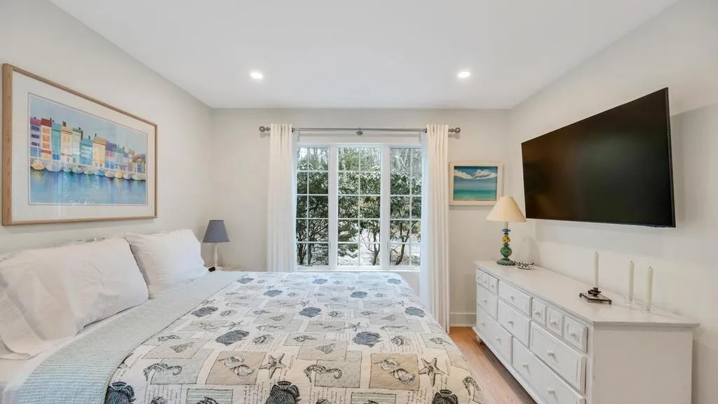 Un dormitorio con una cama, una ventana grande y un televisor sobre una cómoda.