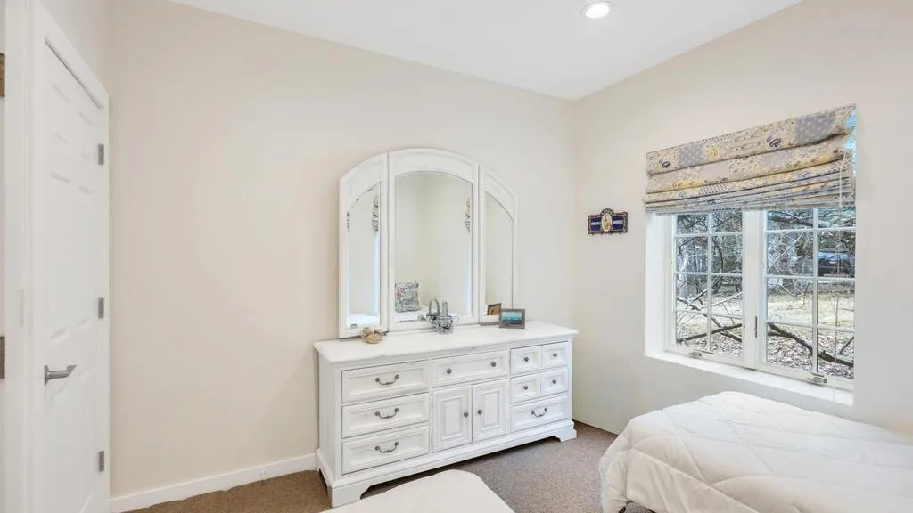 Un dormitorio con una cómoda blanca y una cama junto a la ventana.