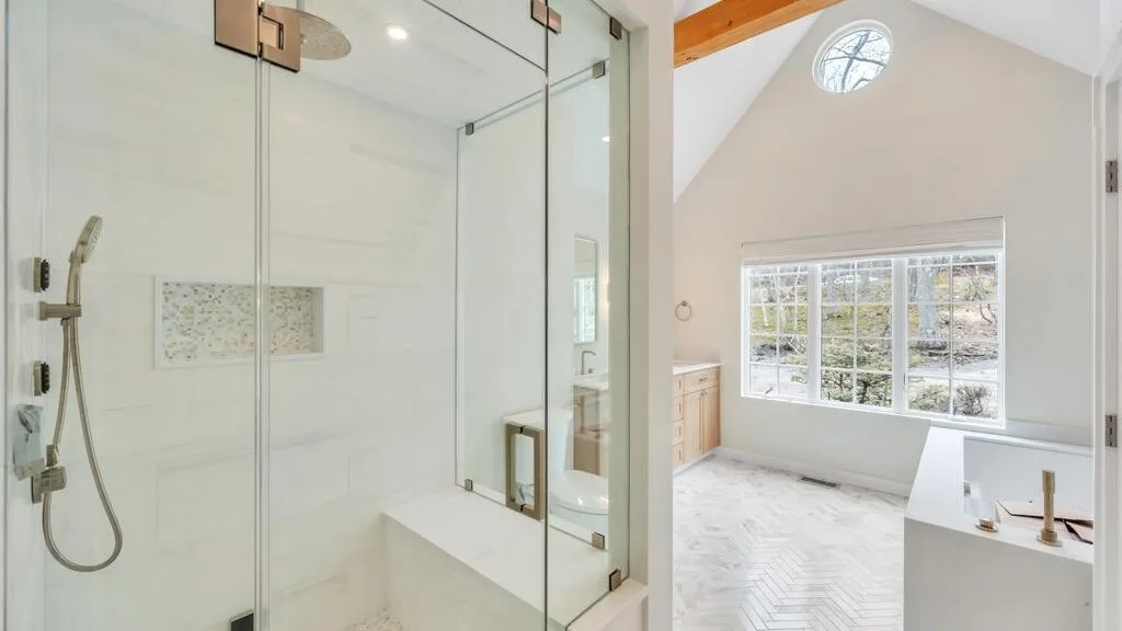 Un baño luminoso con una ducha de vidrio junto a una ventana grande.