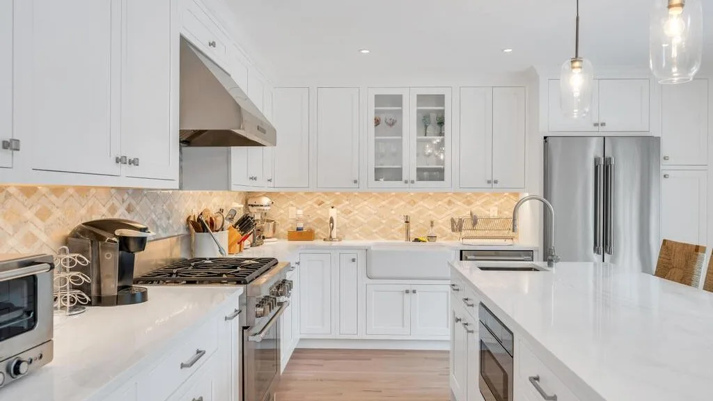Una cocina blanca y luminosa con una isla central y electrodomésticos de acero inoxidable.