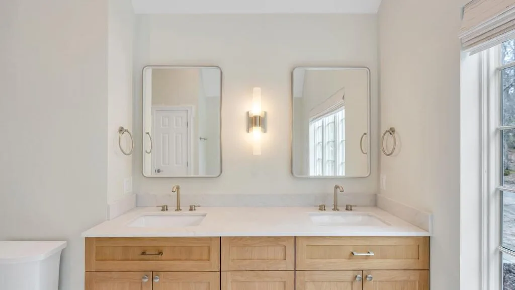 Un baño luminoso con un lavabo doble, dos espejos y una ventana.