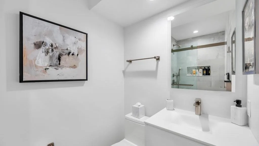 Un tocador de baño luminoso con un espejo amplio y una obra enmarcada.