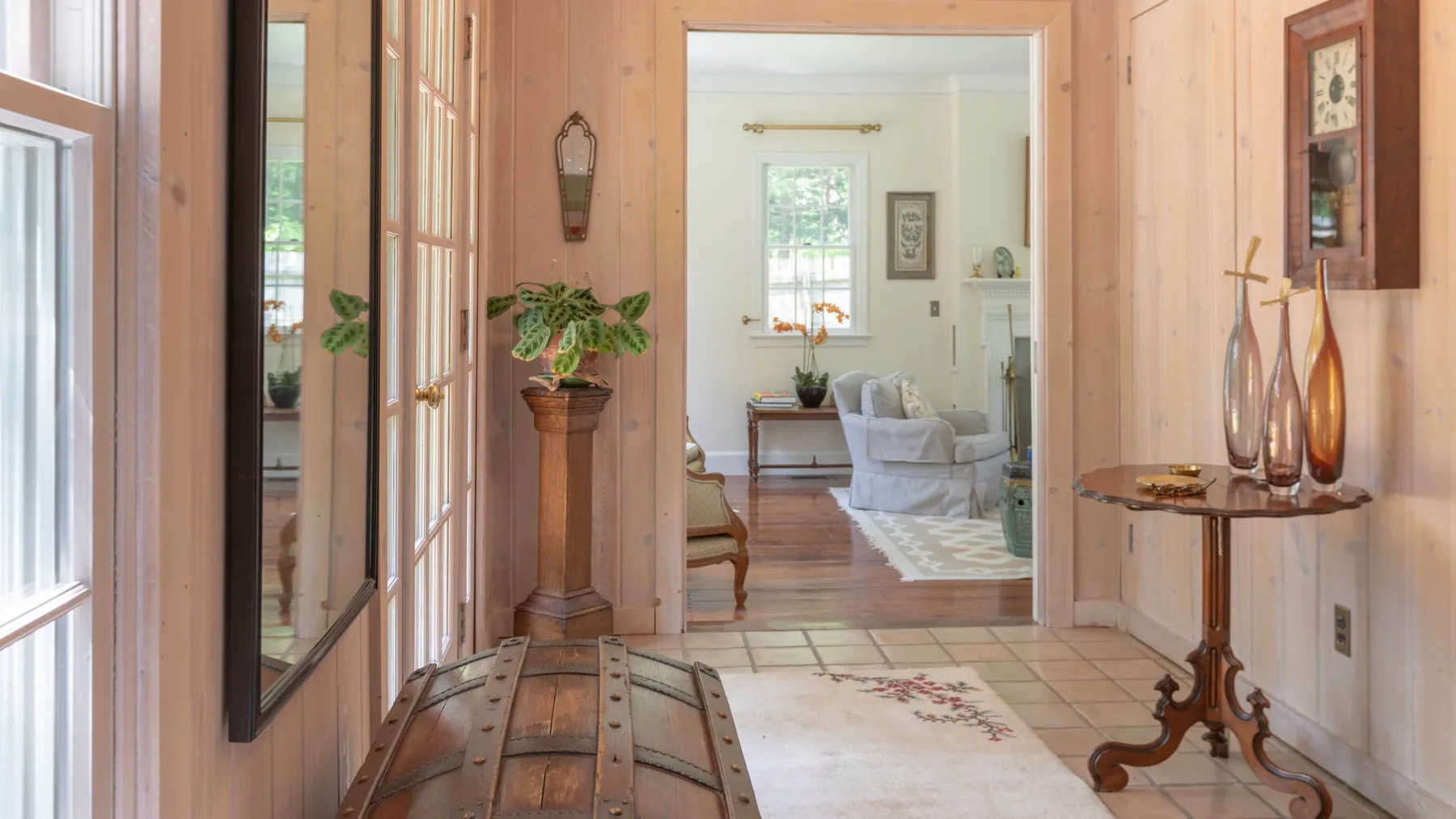 Un pasillo revestido de madera da a una sala luminosa con asientos y una alfombra.