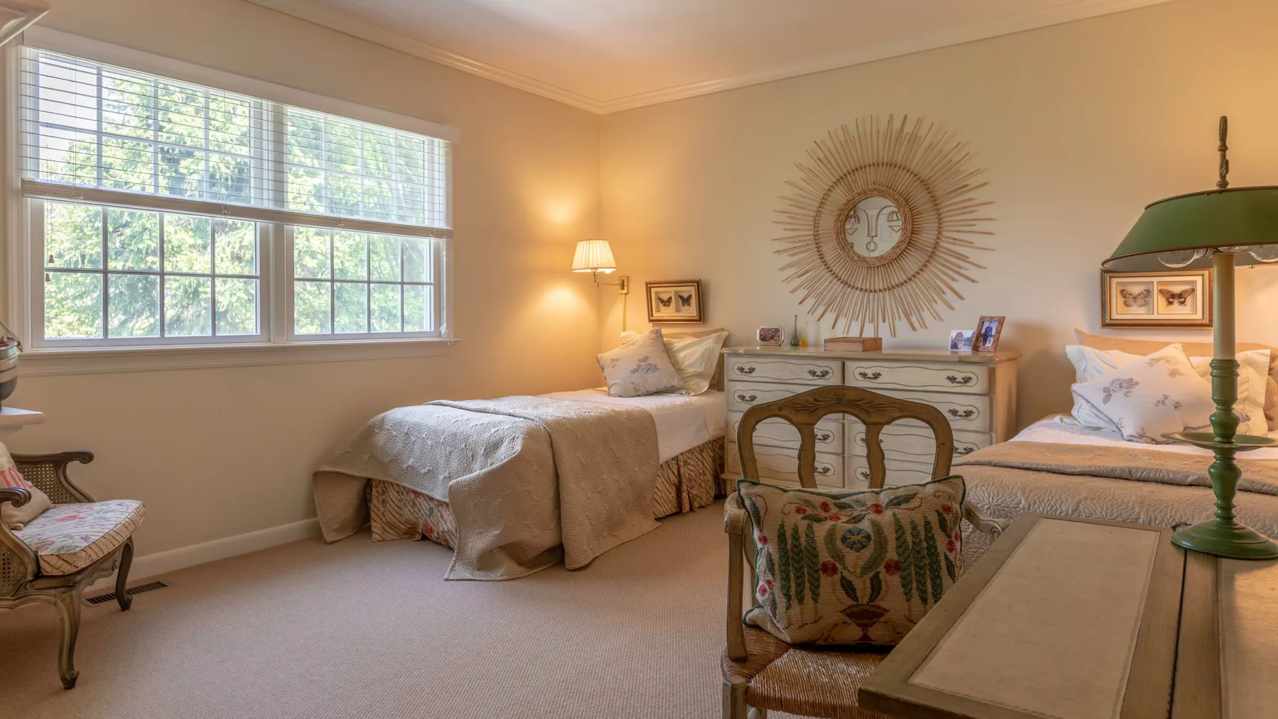 Un dormitorio luminoso con dos camas, una cómoda y una ventana grande.