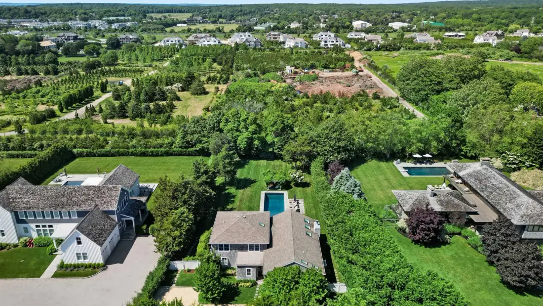 Aerial view of homes and green landscaping, with a swimming pool near the center.