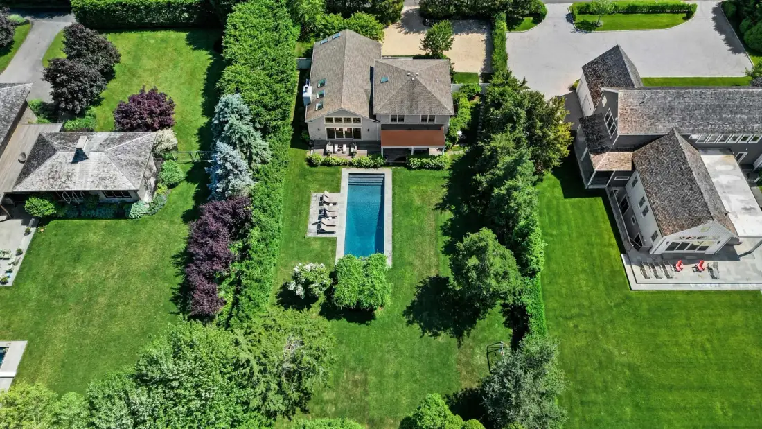An aerial view of a landscaped property with several buildings and a rectangular swimming pool.