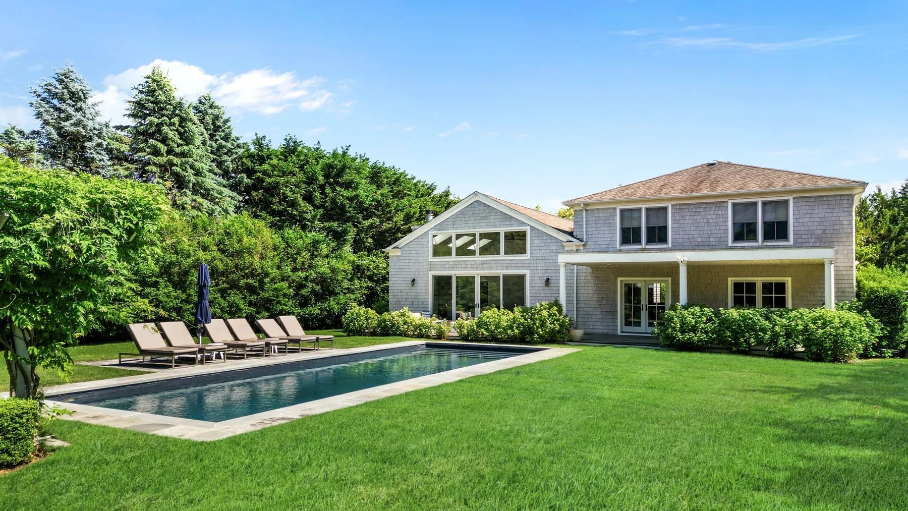 A house and swimming pool beside a broad green lawn.