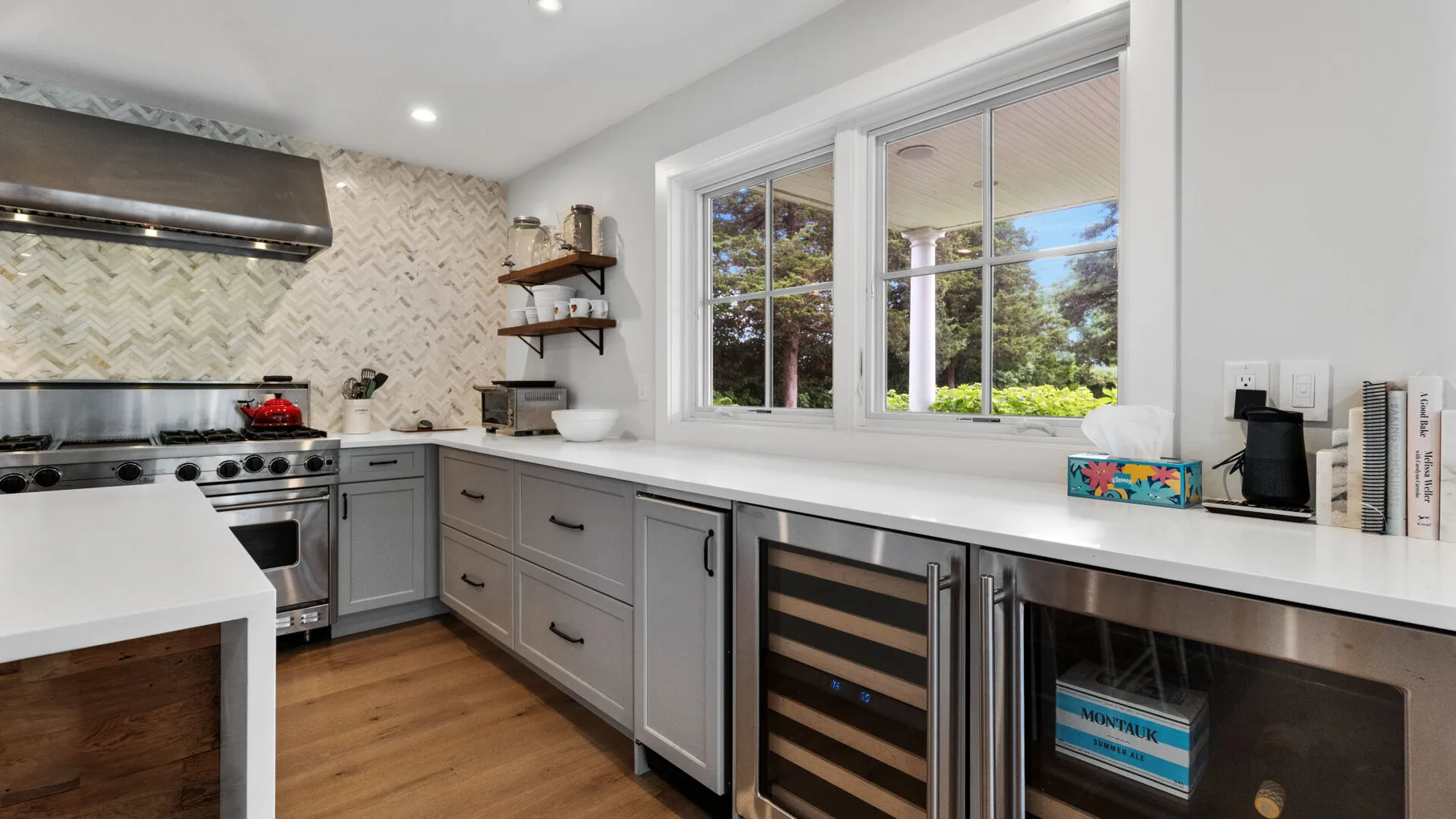 A bright kitchen with gray cabinetry, white counters, and a large window.