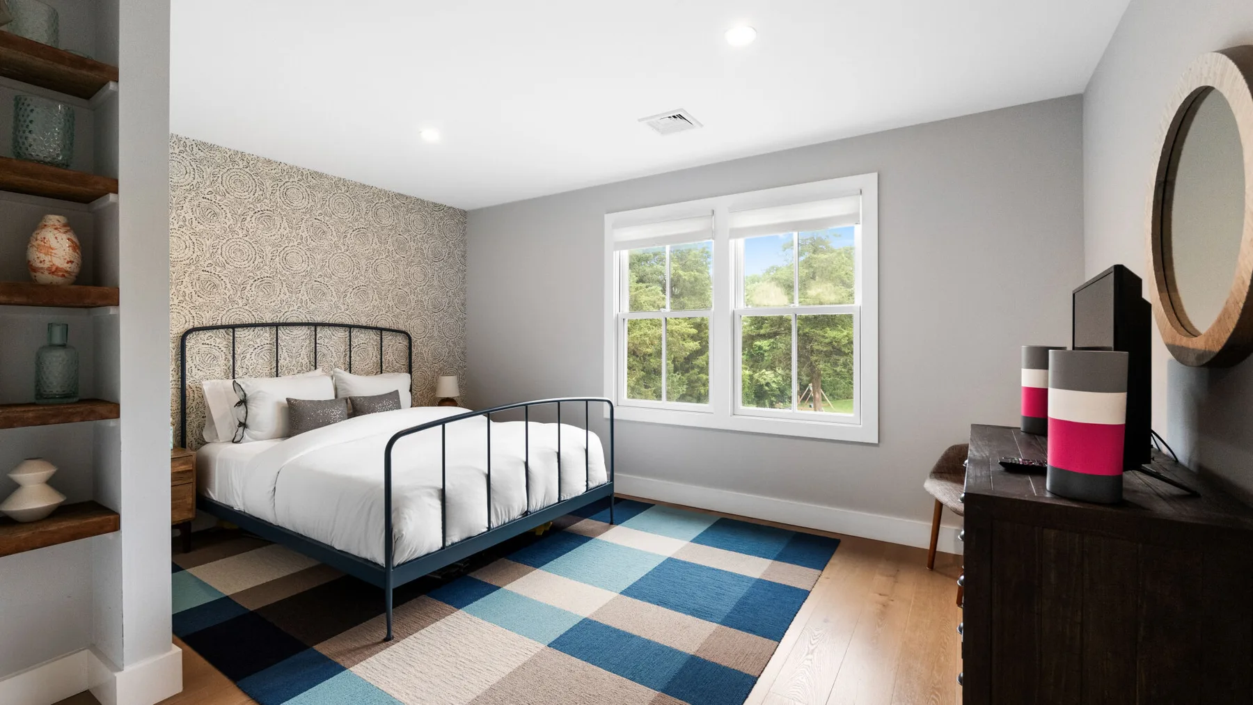 A bedroom with a metal-framed bed, a large window, and a dark dresser.
