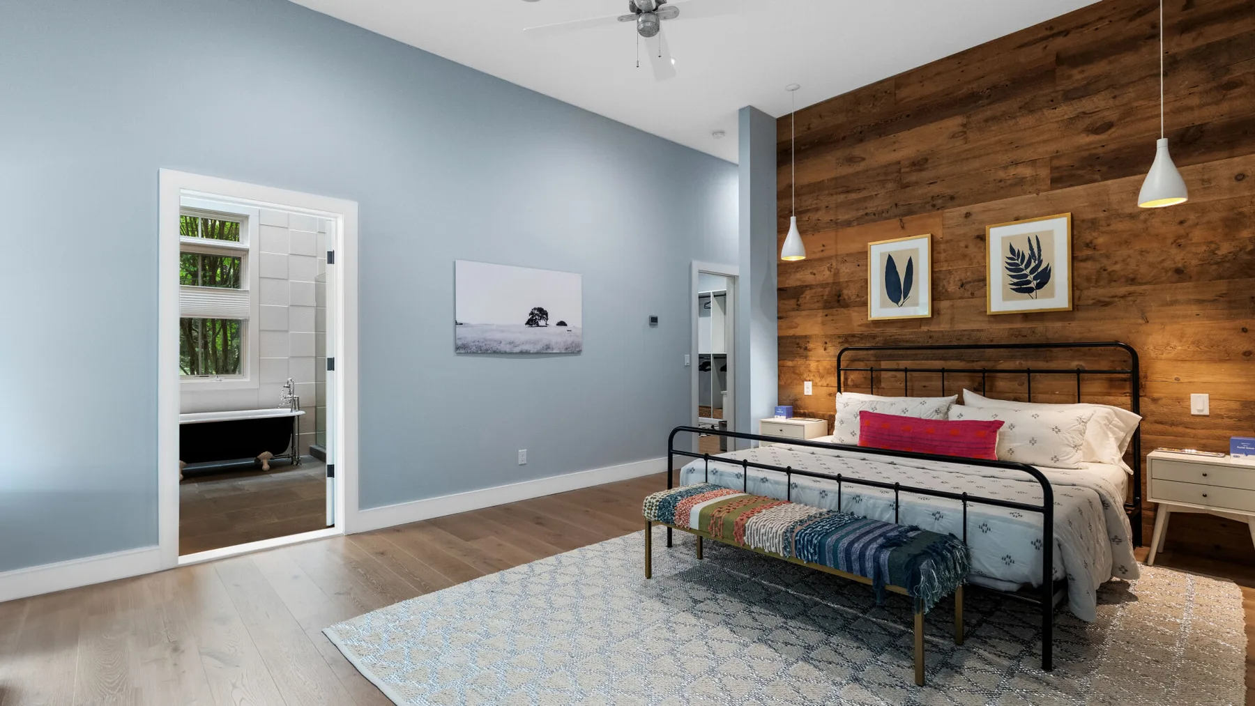 A bedroom features a bed with a colorful bench against a wood-paneled wall.