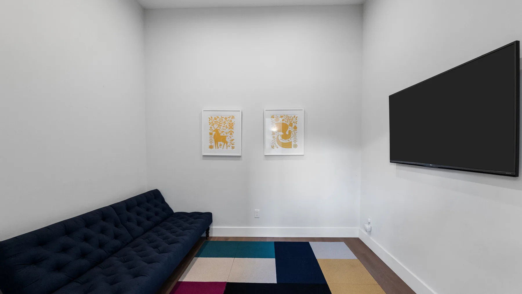A bright living room with a dark sofa and a wall-mounted television.