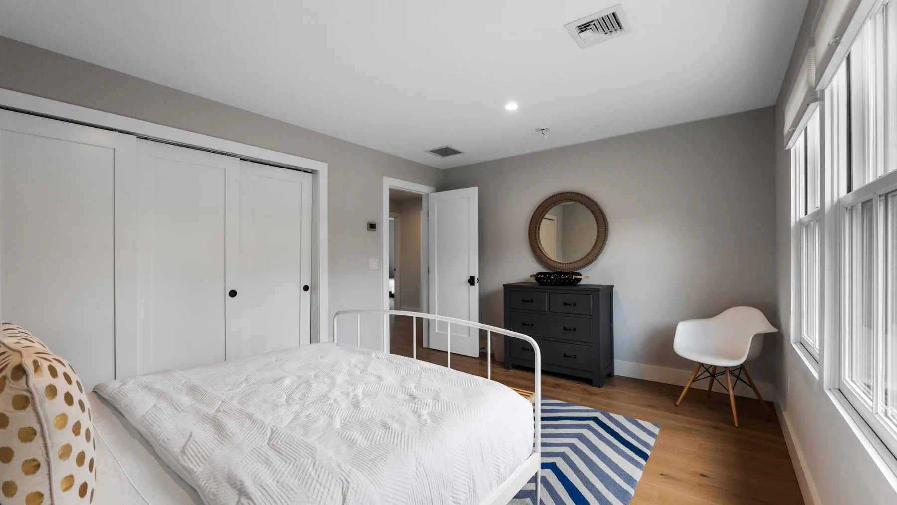 A bright bedroom with a bed, dresser, and large windows.