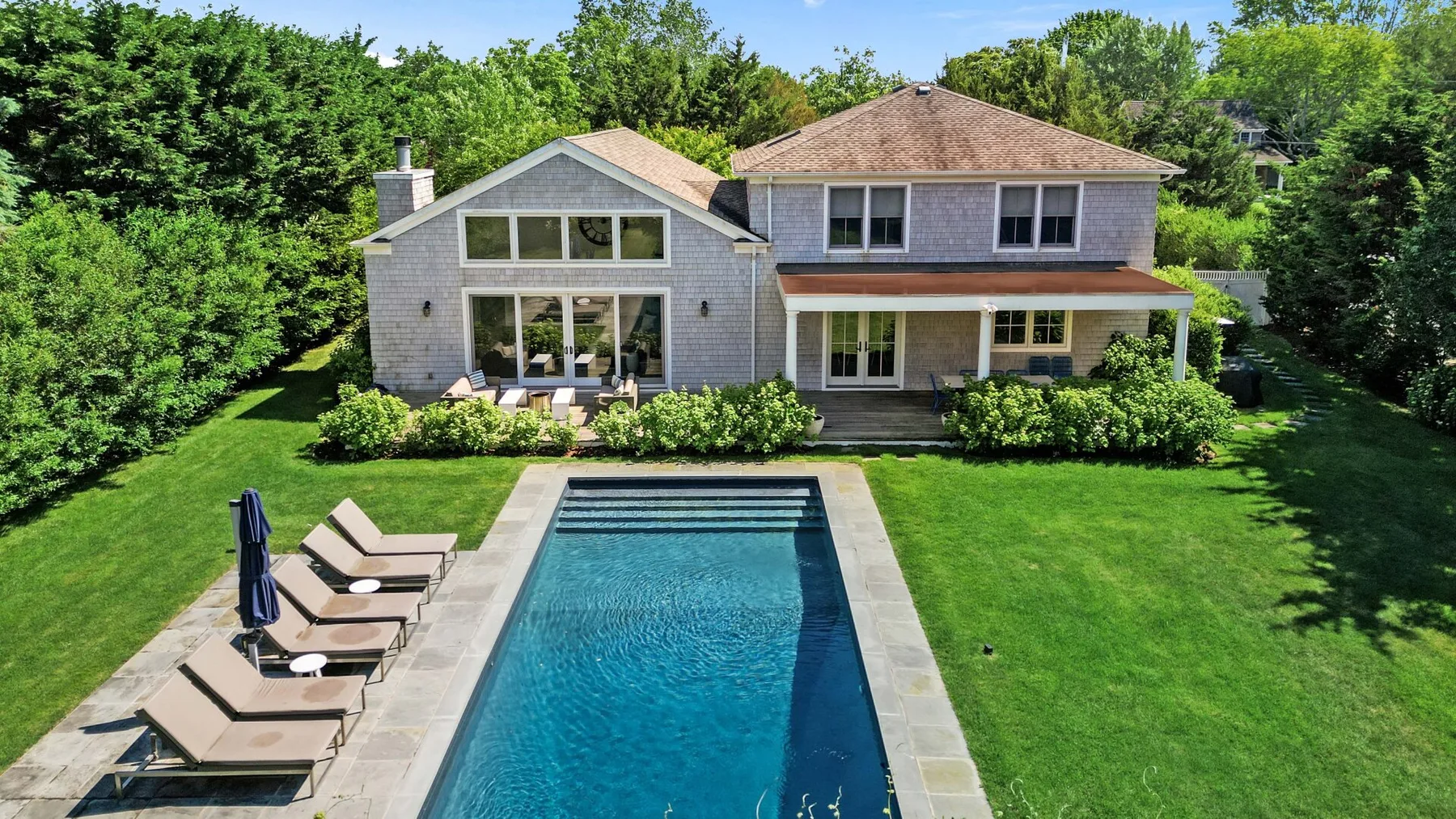 A house with a swimming pool and lounge seating on a green lawn.