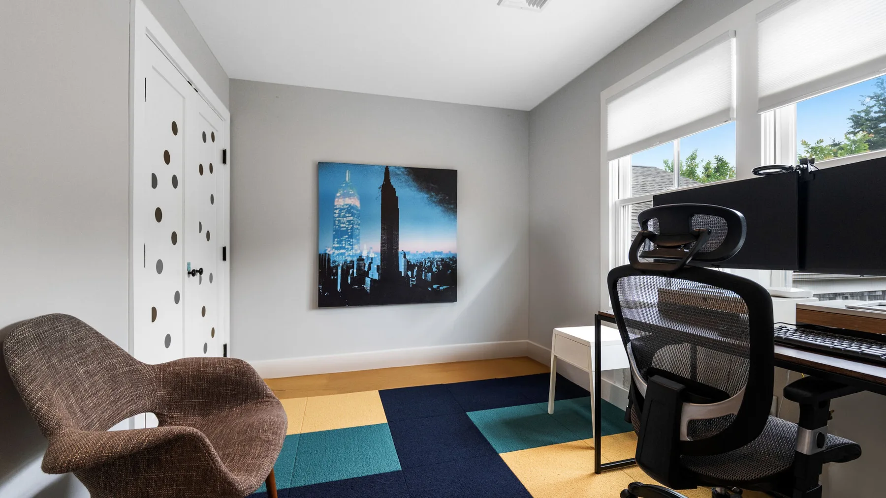 A home office with a desk, computer monitors, and an abstract cityscape print.