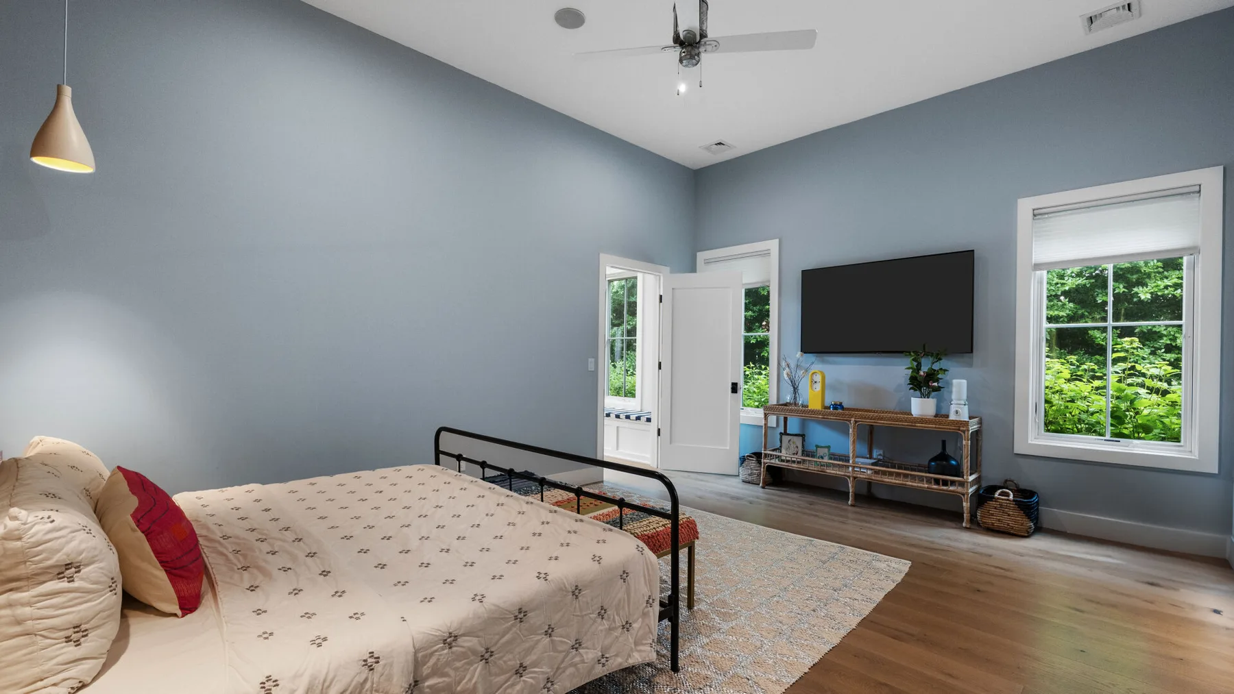 A bedroom with a bed, television, and windows overlooking greenery.