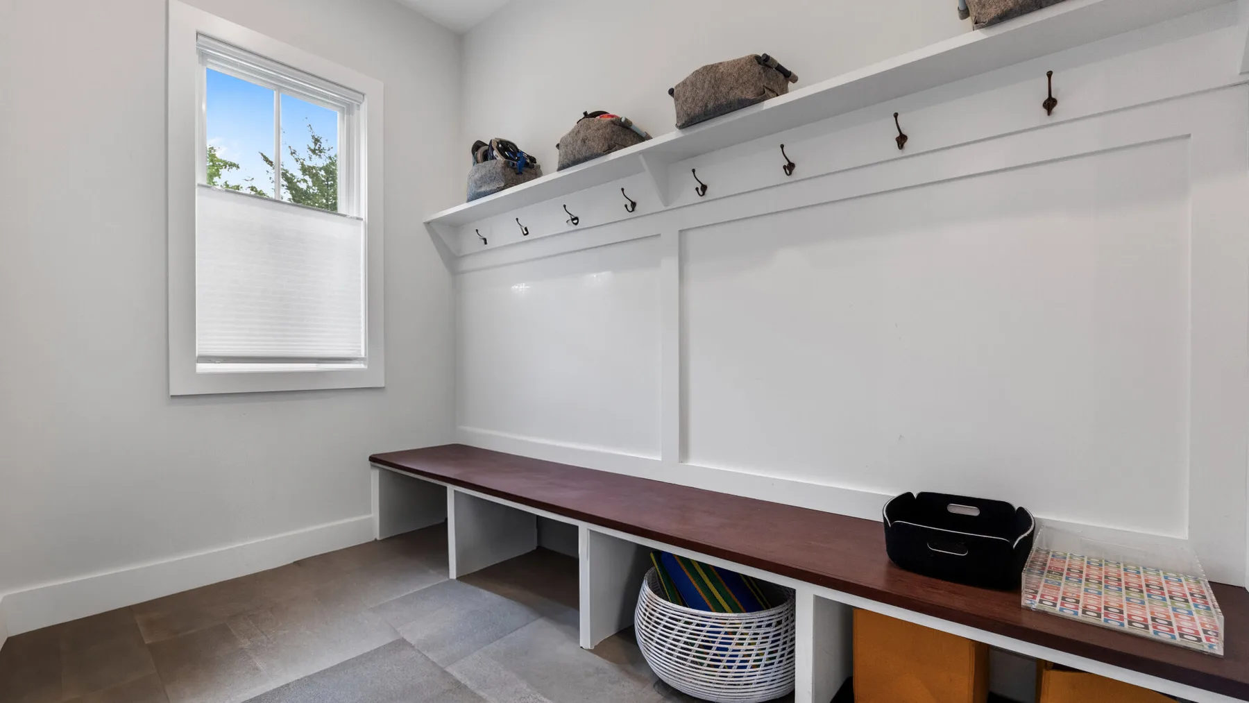A white mudroom features a long bench, wall hooks, and a window.