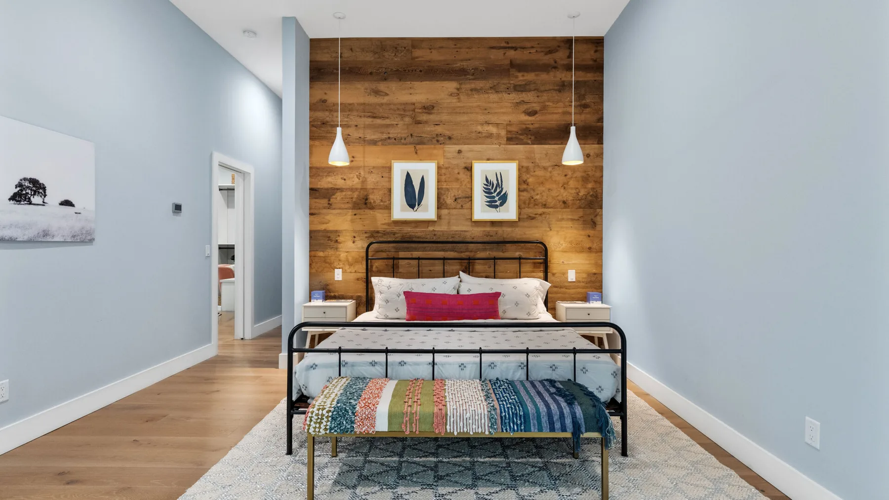 A bedroom with a bed against a wood-paneled wall and two pendant lights.