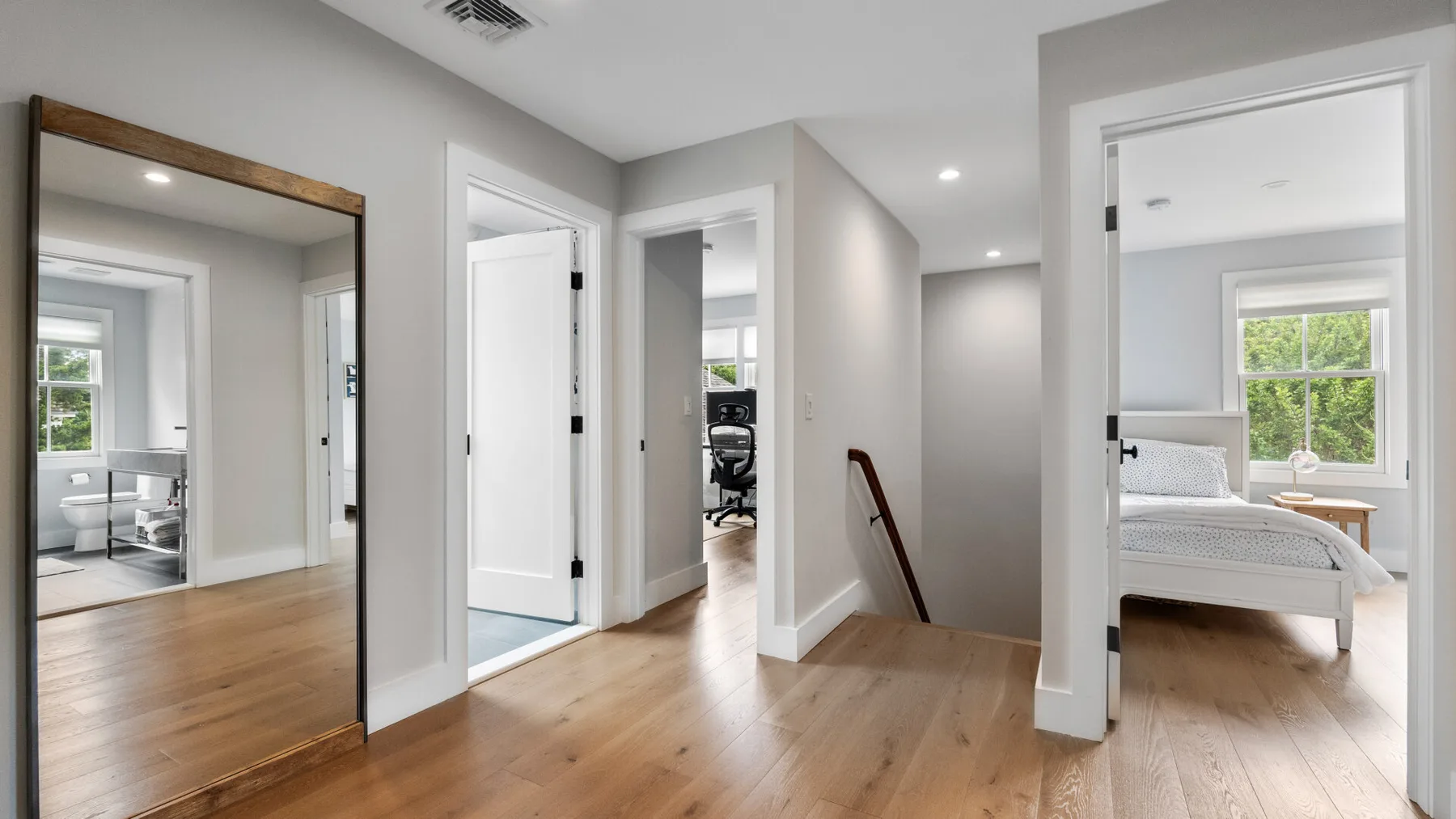 A bright hallway with wood flooring and open doorways to adjoining rooms.