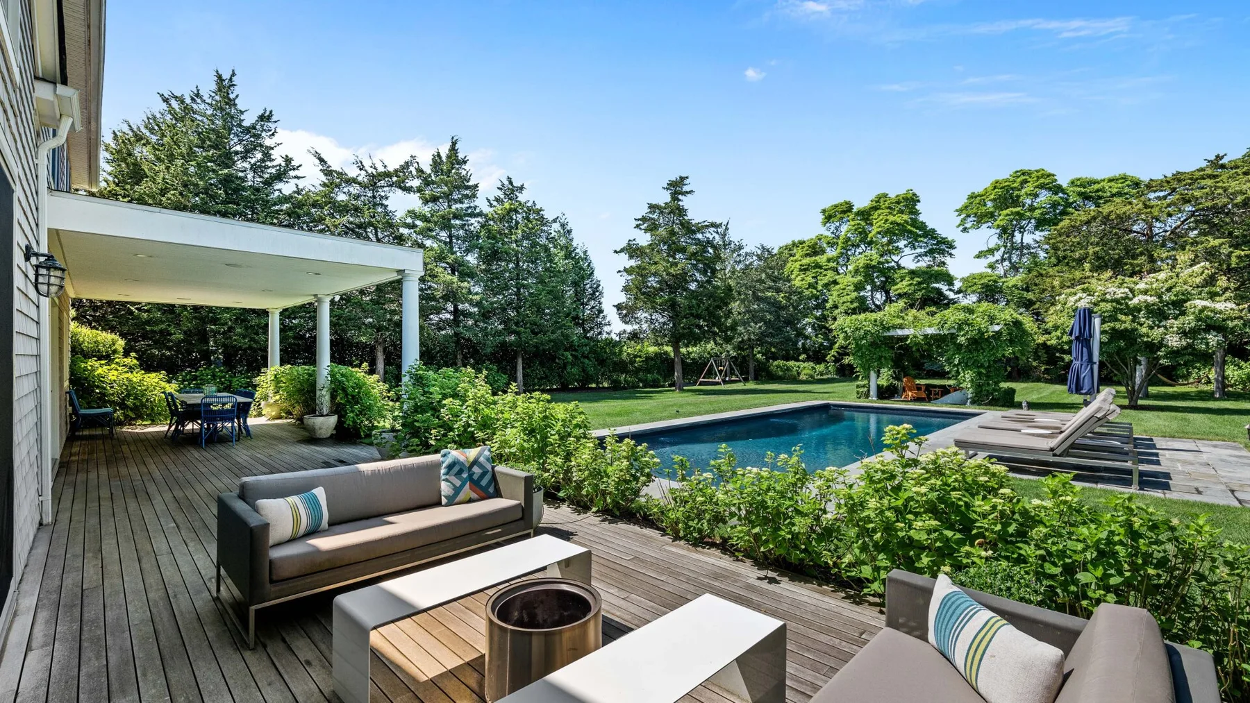 Un patio exterior con asientos da a una piscina y un jardín cuidado.
