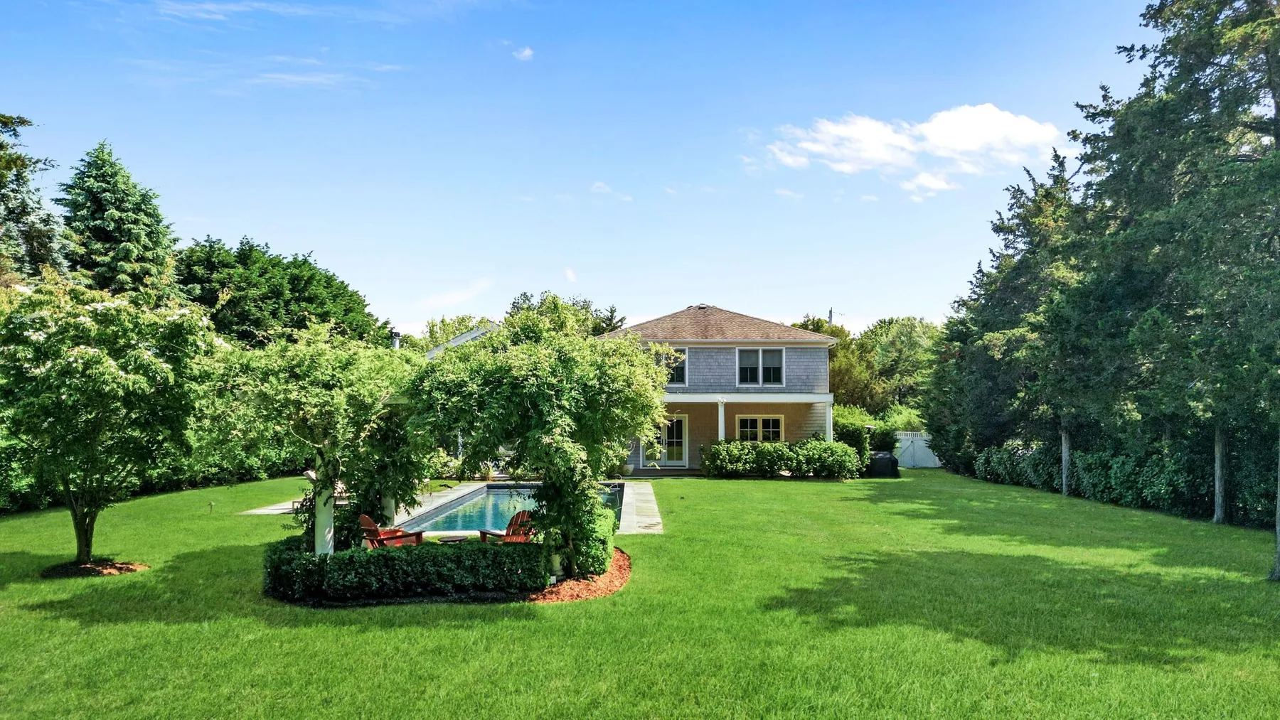 A two-story house stands beyond a broad green lawn, with a small pool in the foreground.