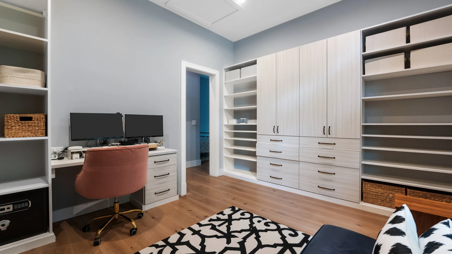 A home office with a desk, monitors, built-in cabinets, and a patterned rug.
