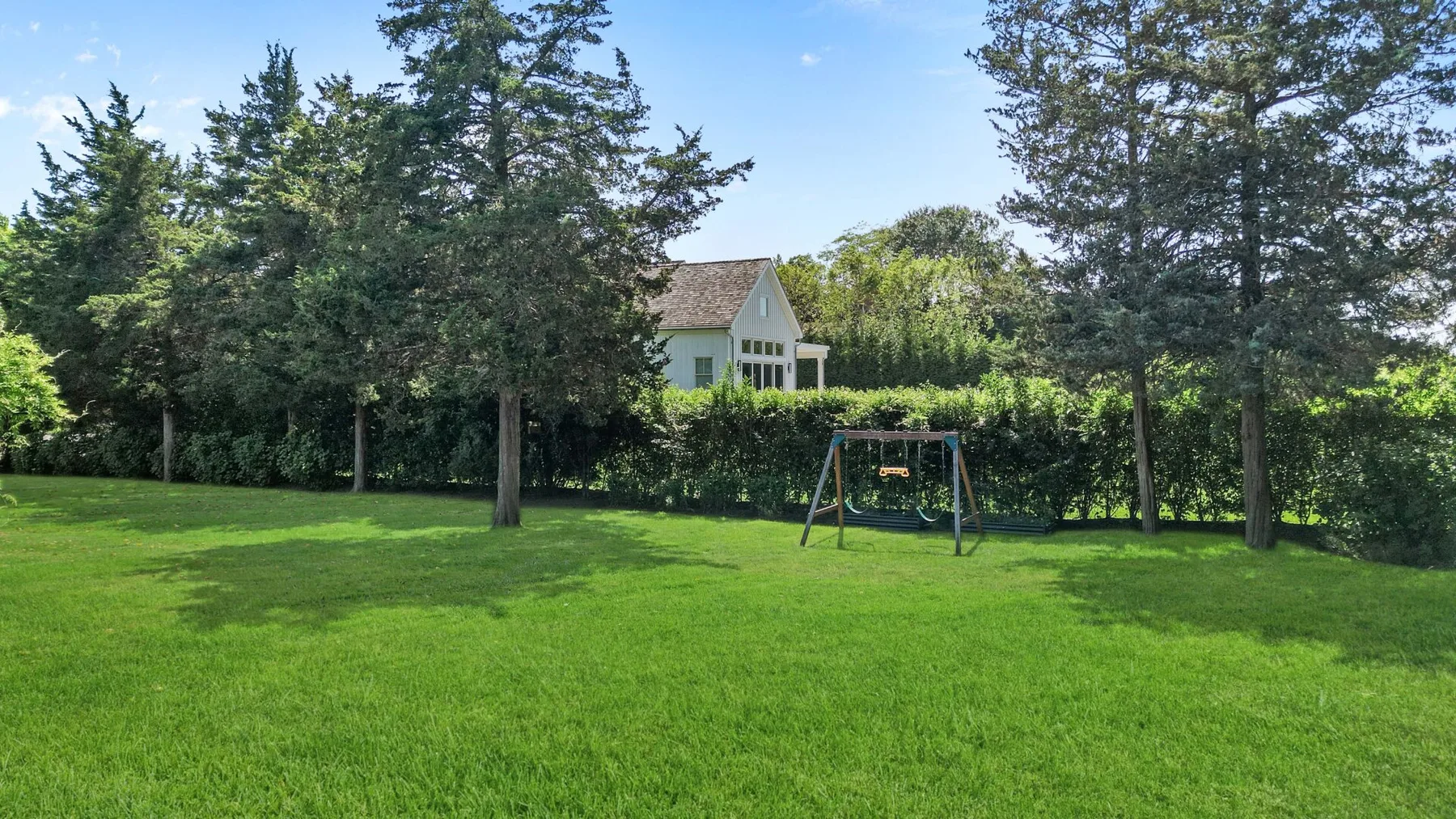 A grassy yard with trees, a hedge, and a swing set.