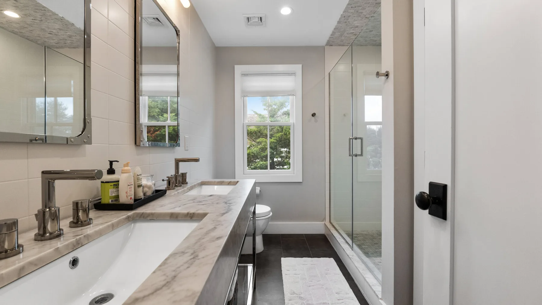 A bright bathroom with a long vanity, a window, and a glass shower.