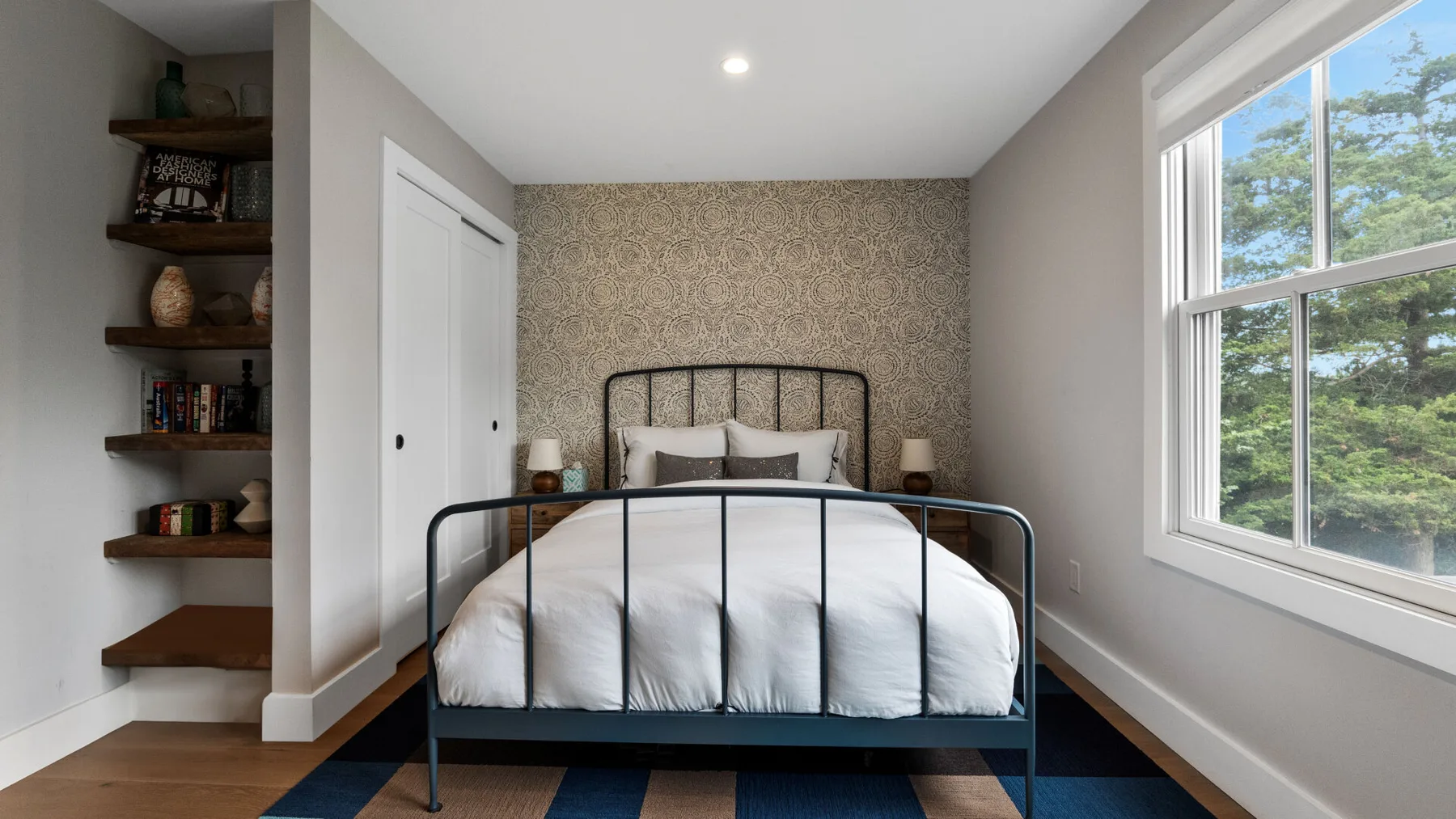 A bedroom with a dark metal bed and a large window.