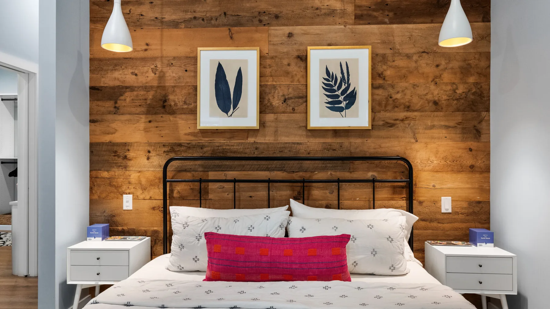 A bedroom with a bed against a wood-paneled wall and framed botanical prints.
