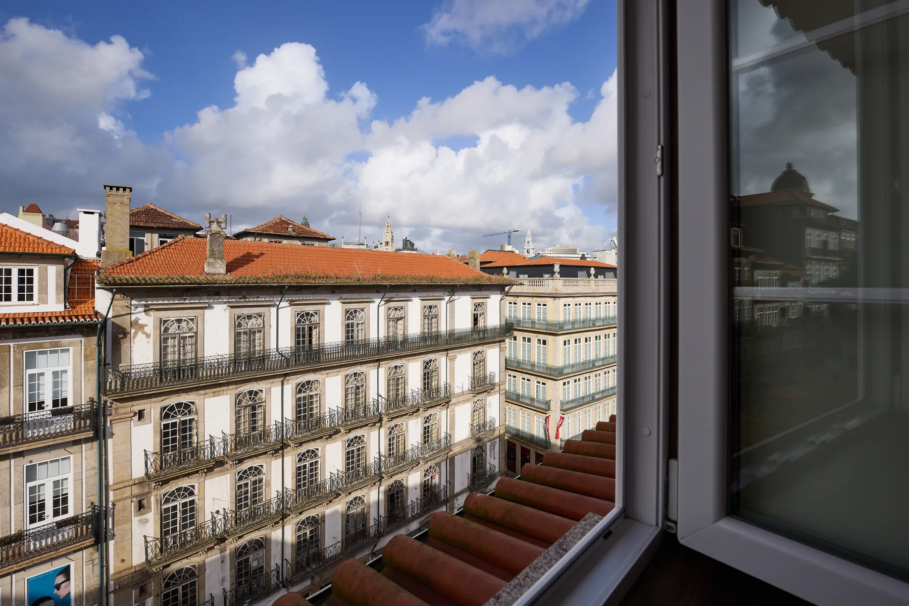 A view of historic city buildings with red-tiled roofs through an open window.