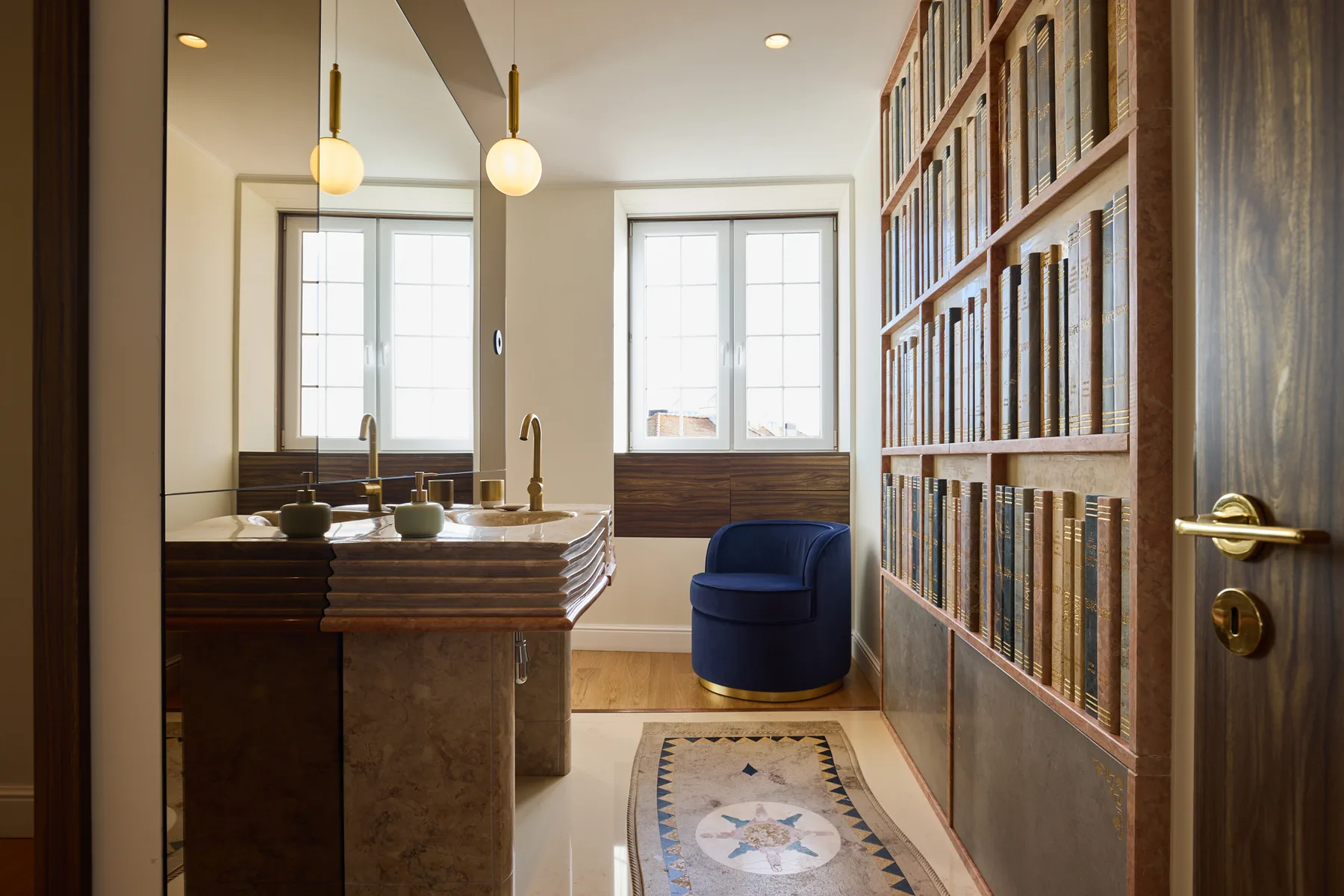 A bathroom with a sink, a blue chair, and a wall of bookshelves.