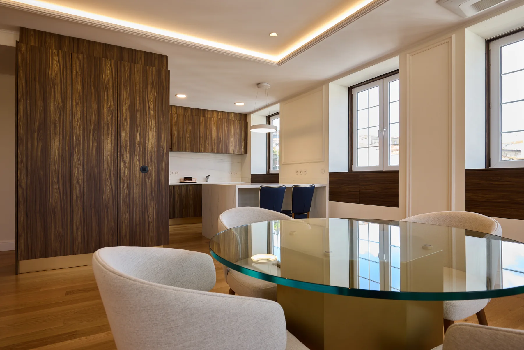 A dining area with a glass table and an open kitchen in the background.