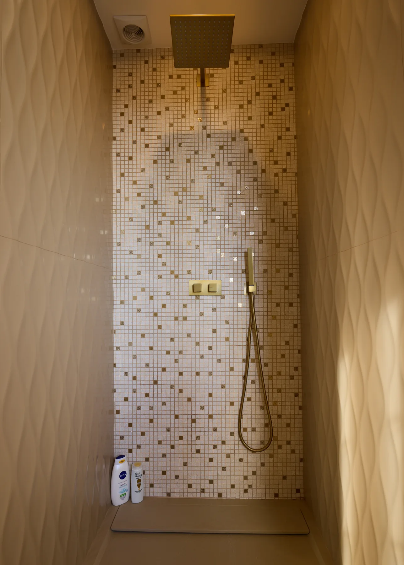 A tiled shower area with a handheld showerhead and controls.