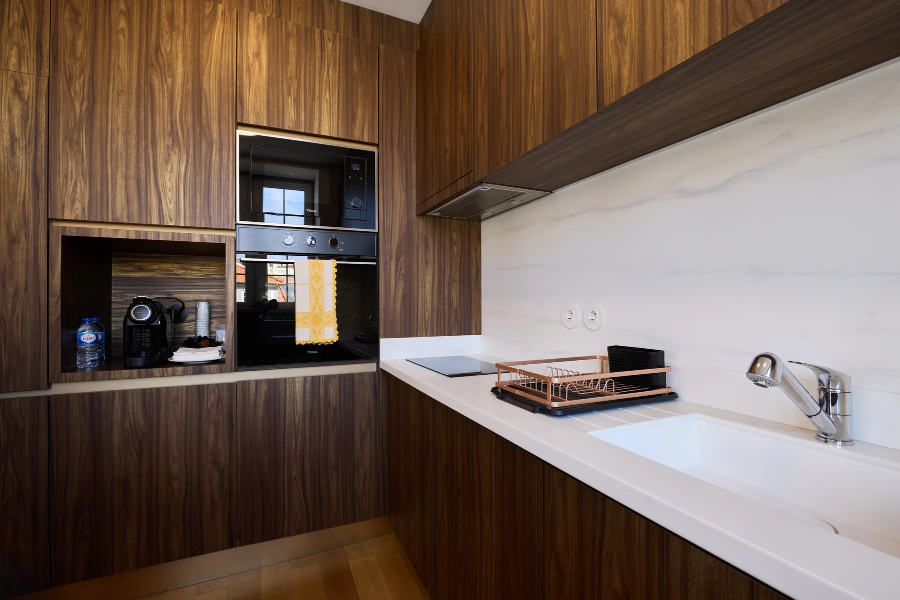 A modern kitchen with dark wood cabinets, a built-in oven, and a sink.