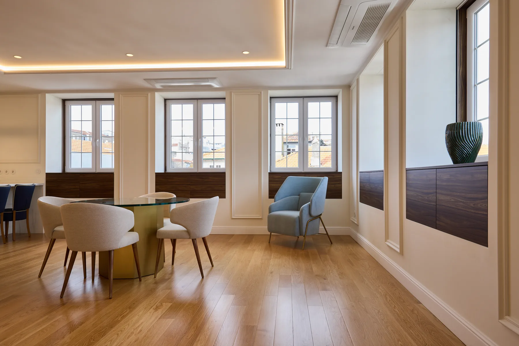 A bright dining and sitting area with a round table, chairs, and windows.