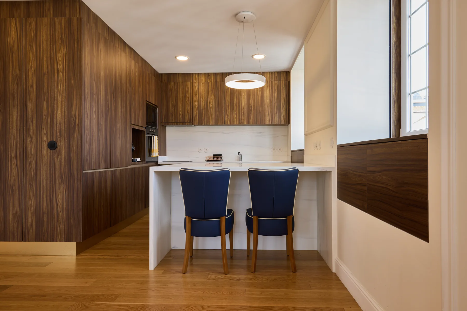 A modern kitchen with a white island and two blue chairs.