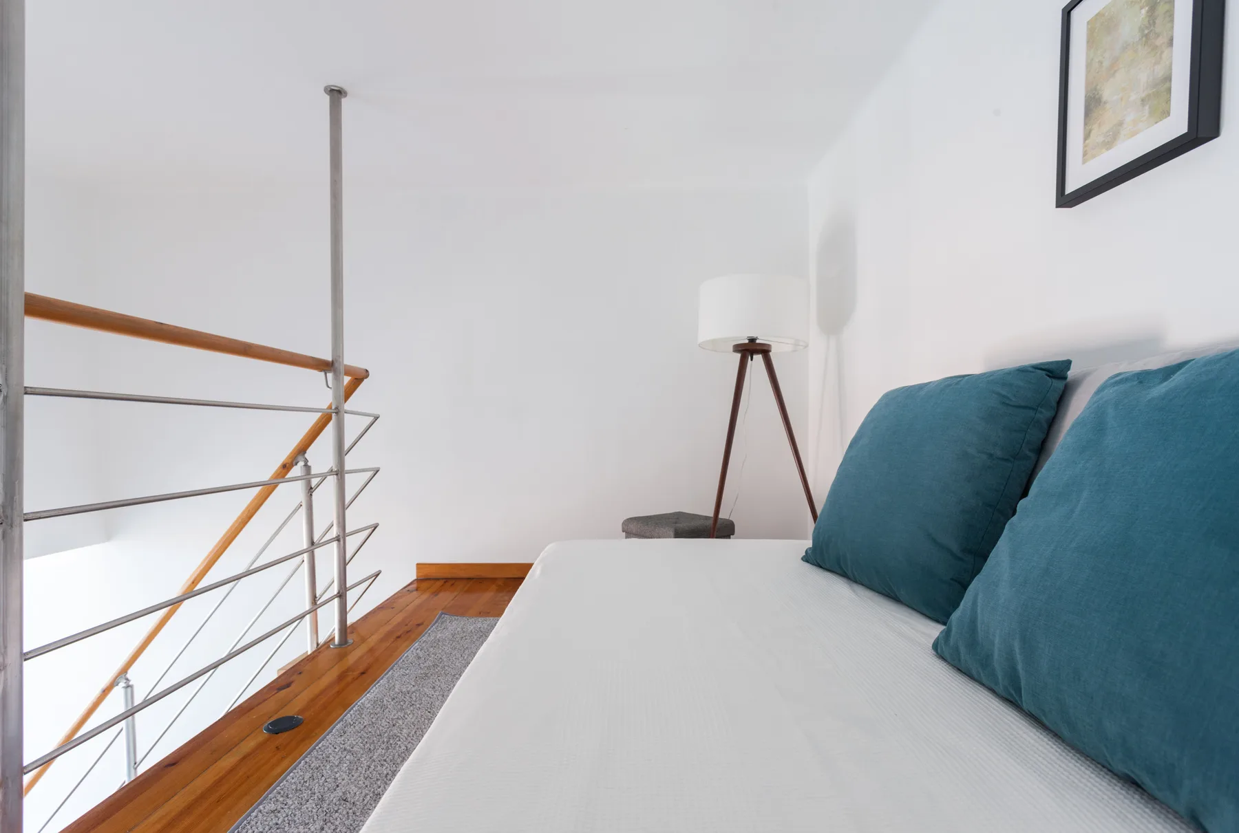 A bright bedroom with a bed, teal pillows, and a railing beside it.