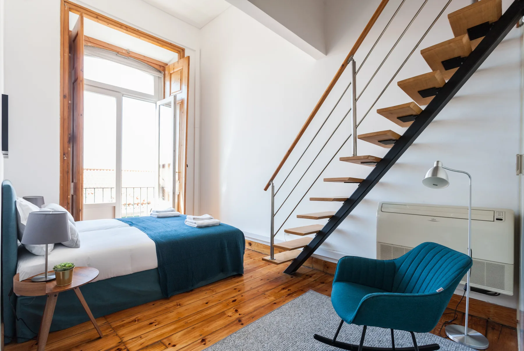 A bedroom with a bed beside a staircase and an open balcony door.