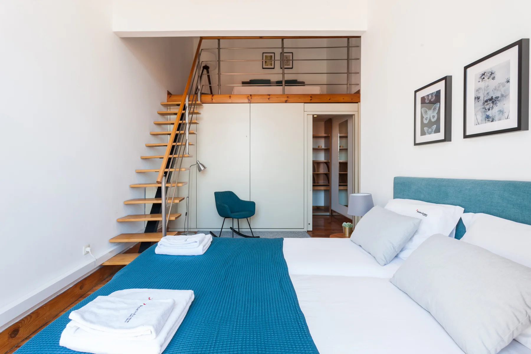 A bedroom with a bed, blue bedspread, and staircase leading to a loft.
