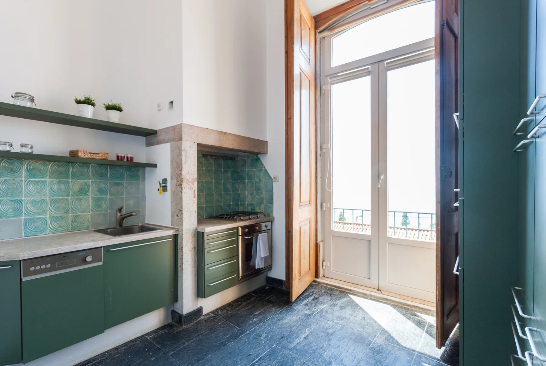A compact kitchen with green cabinets and a tall glass balcony door.