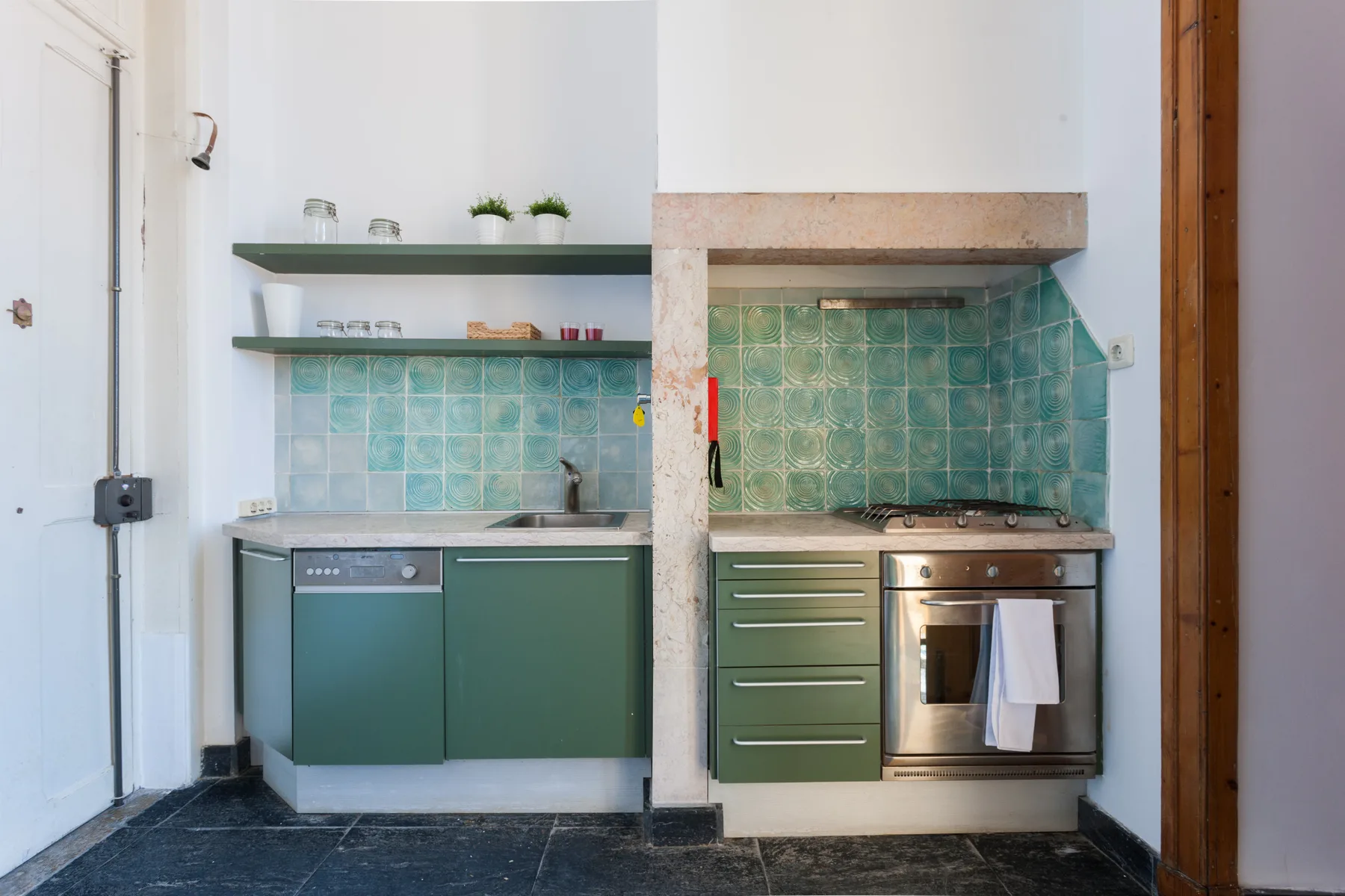 A compact kitchen with green cabinets, tiled backsplash, and open shelves.