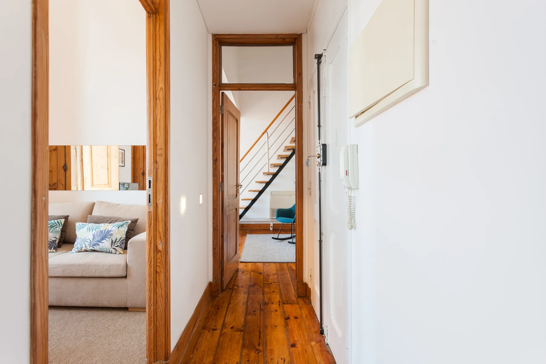 A wooden hallway opens onto a living area with a sofa and staircase.