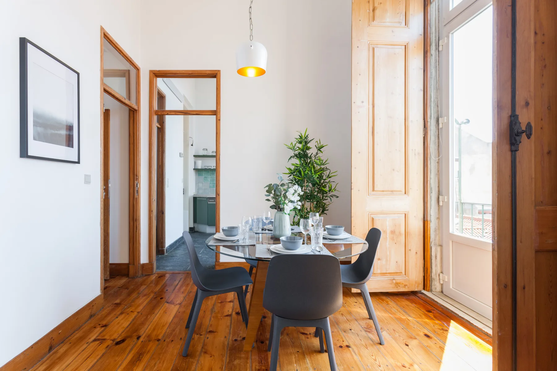 A dining area with a table, chairs, and a potted plant beside tall windows.