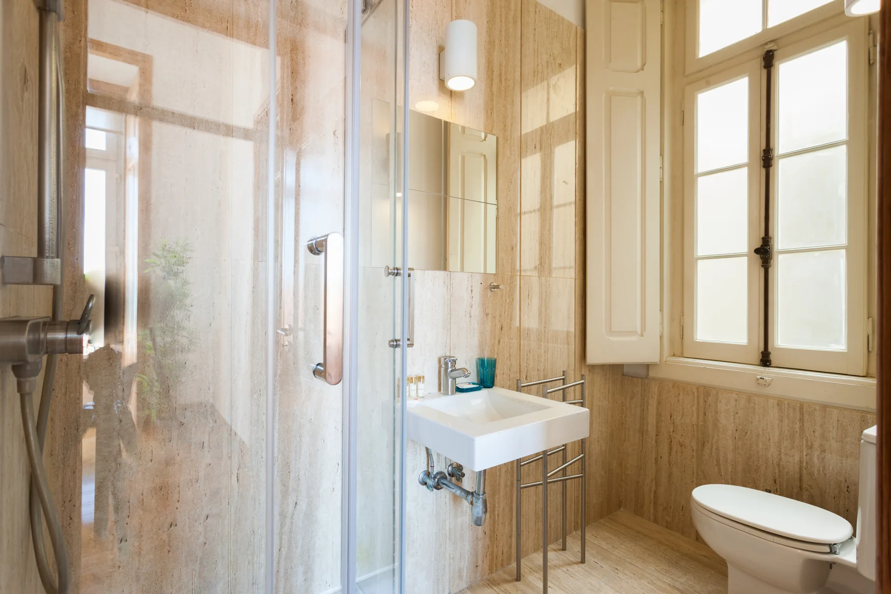 A bathroom with a glass shower, a sink, and a window.