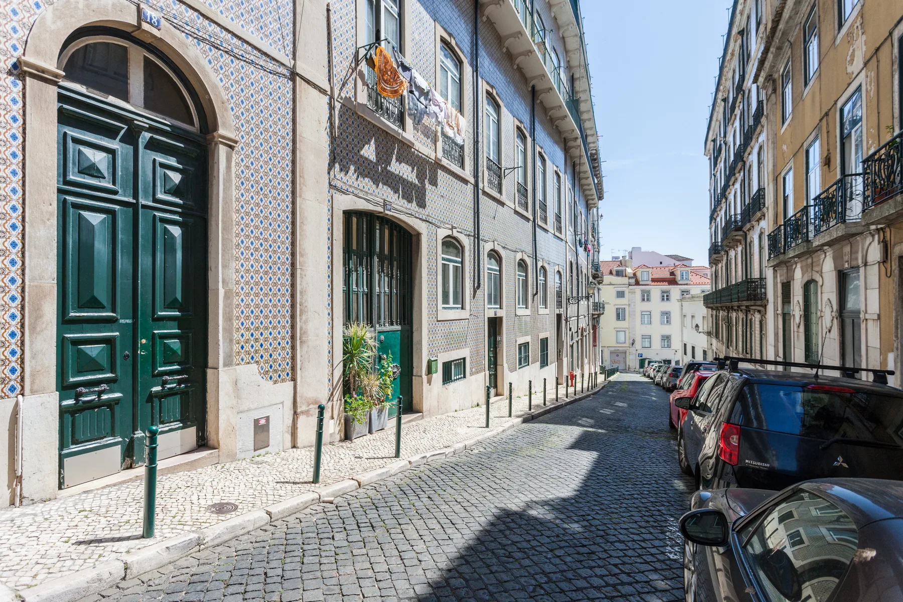 A narrow cobblestone street lined with buildings and parked cars.