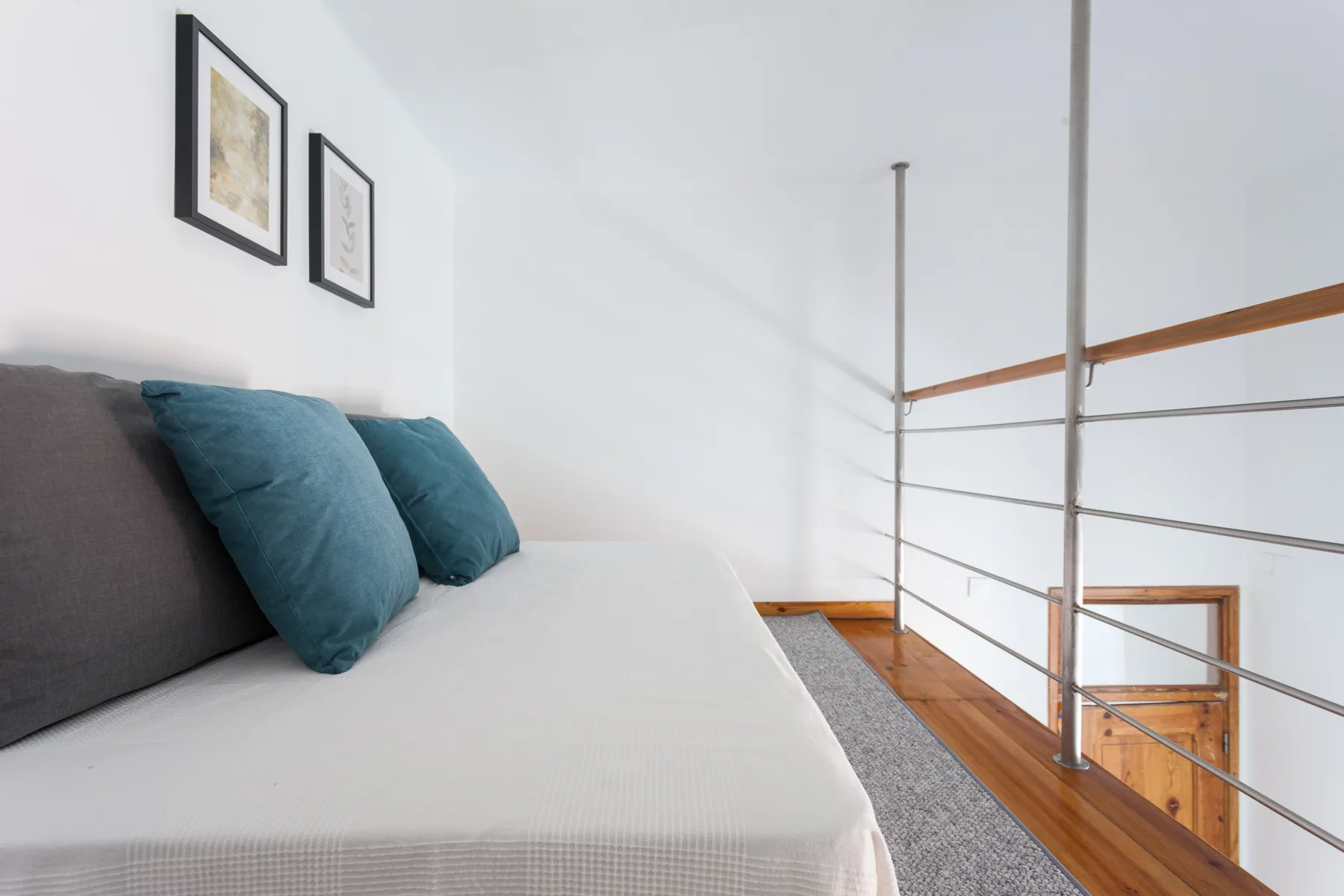 A loft sleeping area with a bed, teal pillows, and a metal railing.